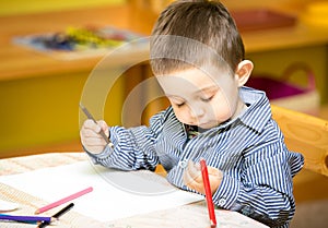 Little child boy drawing with colorful pencils in preschool at table in kindergarten