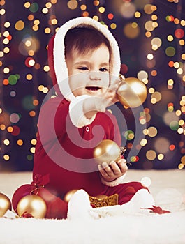 Little child boy dressed as santa playing with christmas decoration, dark background with illumination and boke lights, winter hol