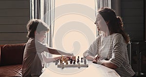 Little child boy enjoying learning playing chess with mum.