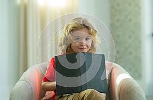 Little child boy lying on the couch at home and reading a childrens story book. Concept of education, childhood, book