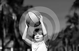 Little child boy playing basketball with basket ball. Kid with basket ball on sky background, cheerful and pleasant.