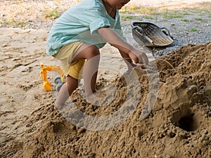 Little child boy playing and climbing sand pile outdoor with dirty foot, hand.