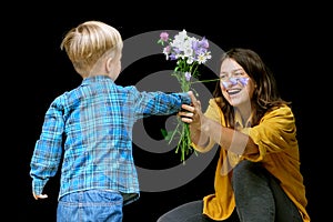 Little child boy present mother bouquet of wild flowers. Son greeting mom with birthday or mother`s day