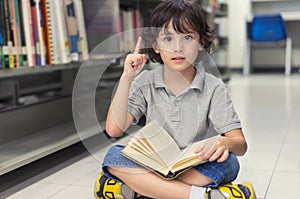 Little child boy reading a book and finger pointing up.