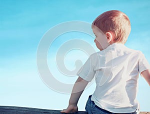 Little child boy sitting pensive looking away outdoors over blue sky on sunset