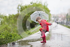Little child boy with an umbrella playing out in the rain