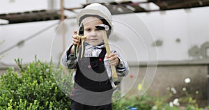 Little child builder in a white helmet shows a hammer and pliers at the camera.