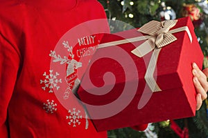 Little child by the Christmas tree with his Christmas gift. Little kid is holding gift box in his hand. Happy new year. Christmas