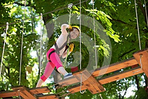 Little child climbing in adventure activity park with helmet and safety equipment. Happy child climbing in the trees.