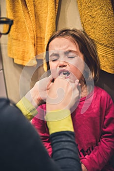 Little child is crying while mother brushes her teeth.