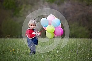 Little child, cute boy on a spring cold windy rainy day, holding colorful balloons in a field, running