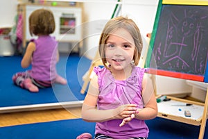 Little child is drawing with color chalk on the chalk board