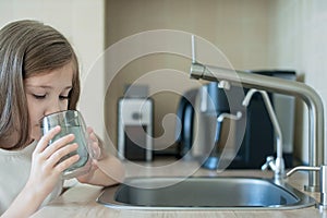 Little child is drinking fresh and pure tap water from glass. Water being poured into glass from kitchen tap. Zero waste and no