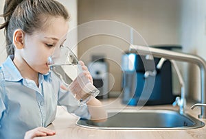 Little child is drinking fresh and pure tap water from glass. Water being poured into glass from kitchen tap. Zero waste and no