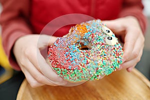 Little child eating funny colorful donut in a street cafe while walking in the city center