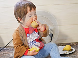 Little child eats a pear. child boy eating fruits at a high stoic. in the kitchen