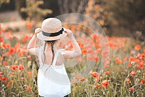 Little child girl 3-4 year old wear white dress and straw hat with boy in poppy meadow outdoors. Kid looking forward back view.