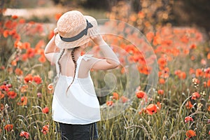 Little child girl 3-4 year old wear white dress and straw hat with boy in poppy meadow outdoors. Kid looking forward back view. Sp