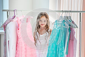 Little child girl choosing her clothes. Kid thinking what to choose to wear in front of many choices of dresses on hangers