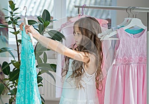 Little child girl choosing her clothes. Kid thinking what to choose to wear in front of many choices of dresses on hangers