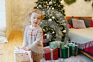 Little child girl with christmas gift box at home near christmas tree