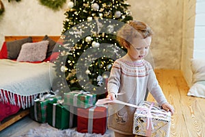 Little child girl with christmas gift box at home near christmas tree