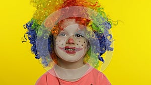 Little child girl clown in colorful wig making silly faces, having fun, smiling, dancing. Halloween