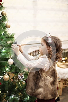 Little child girl decorating Christmas tree with balls at home, indoors. Close up. Christmas concept