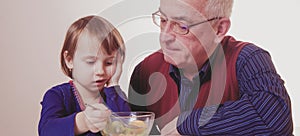 Little child girl does not want to eat and has no appetite. Grandpa feeding his grandchild with fruits salad