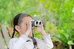 Little child girl in a field looking through binoculars in nature outdoor. Explore and adventure concept