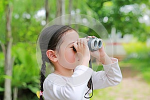 Little child girl in a field looking through binoculars in nature outdoor. Explore and adventure concept