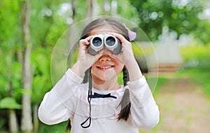 Little child girl in a field looking through binoculars in nature outdoor. Explore and adventure concept