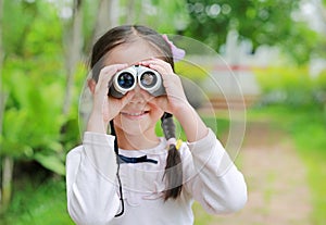 Little child girl in a field looking through binoculars in nature outdoor. Explore and adventure concept