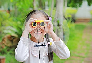 Little child girl in a field looking through binoculars in nature outdoor. Explore and adventure concept