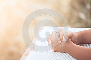 Little child girl hands folded in prayer on a Holy Bible