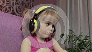 Little child girl in headphones enjoying listen music. Dancing on sofa at home