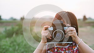 Little child girl holding medium format film camera and taking photo of sunset landscape with green field background