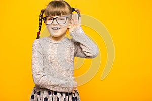 Little child girl journalist in glasses with surprised euphoria face and funny pigtails listening to something holding his hand to