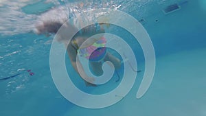 Little child girl learns to swim underwater in a swimming pool