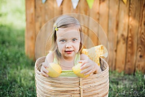 Little child girl with lemons at lemonade stand in park. Portrait of funny baby in basket with fruits