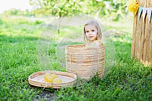 Little child girl with lemons at lemonade stand in park. Portrait of funny baby in basket with fruits
