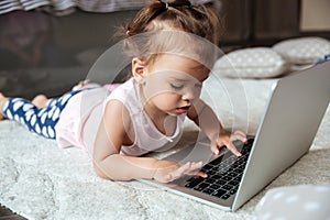 Little child girl lies on bed indoors using laptop computer