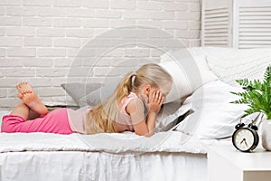 Little child girl lies in bed uses digital tablet.