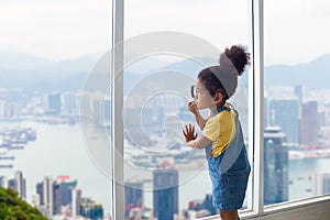 Little child girl with magnifying glass looking outside through the window, Kid standing and looking through the window with