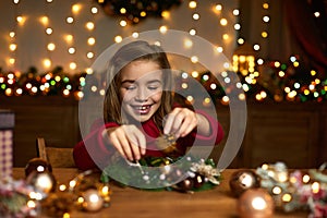 Little child girl makes a handmade Christmas wreath