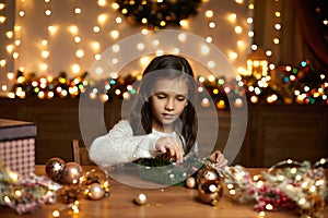 Little child girl makes a handmade Christmas wreath