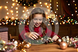 Little child girl makes a handmade Christmas wreath