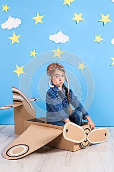 Little child girl in a pilot`s costume is playing and dreaming of flying over the clouds.