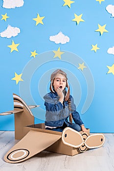 Little child girl in a pilot`s costume is playing and dreaming of flying over the clouds.