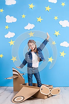 Little child girl in a pilot`s costume is playing and dreaming of flying over the clouds.